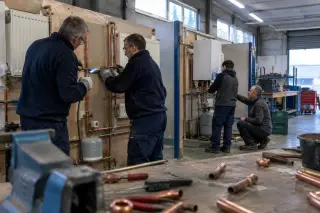 Deux adultes brasent un tuyau de cuivre dans un atelier de formation plomberie et chauffage, près d’un formateur