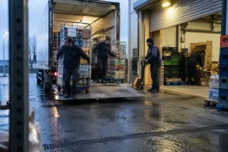 Livraison au petit matin au quai d’un supermarché : des employés déchargent des rolls d’un camion