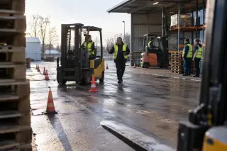 Une stagiaire conduit un chariot élévateur entre des plots sur l’aire de formation d’un centre, un formateur à ses côtés